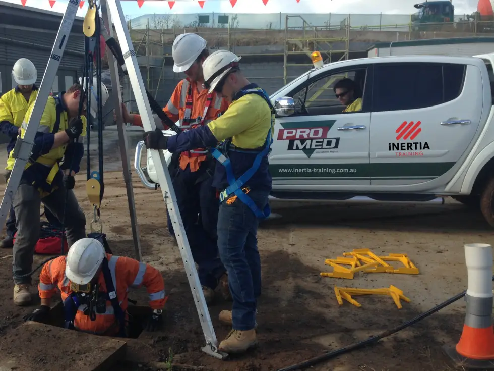 Trainees using a tripod and harness to rescue a worker from a confined space beside a training vehicle