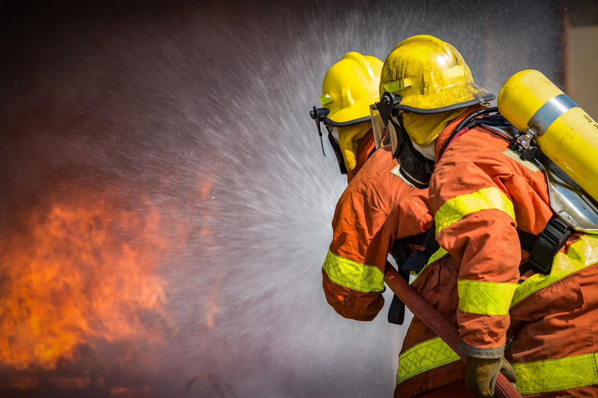 Two firefighters in breathing apparatus using a hose on a fire